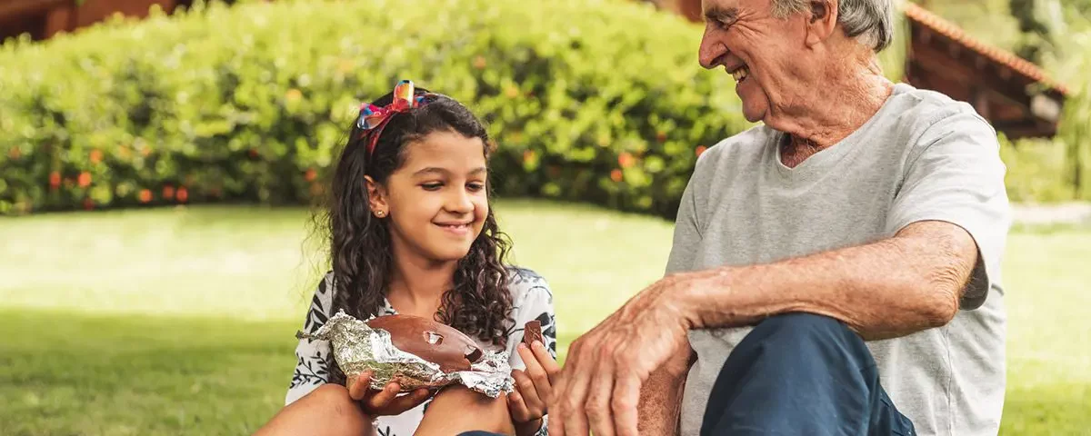 A grandfather and granddaughter sitting on the grass eating chocolate