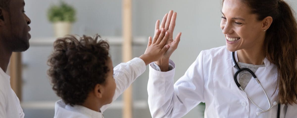 Smiling young female pediatrician give high five to little african American boy at consultation in clinic, happy woman doctor consult biracial toddler kid in hospital. Children healthcare concept